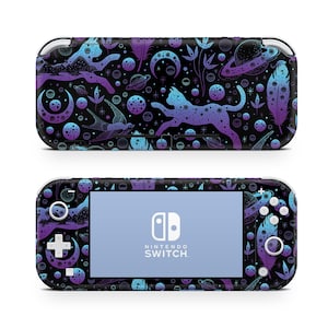 May include: A black Nintendo Switch Lite console with a custom skin featuring a celestial design. The skin has a repeating pattern of planets, moons, feathers, and a cat silhouette in shades of blue and purple. The Nintendo Switch logo is visible on the screen.