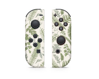 May include: A pair of white Nintendo Switch Joy-Con controllers with a green fern pattern. The controllers have black buttons and a black analog stick.