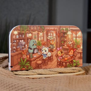 May include: A rectangular decorative panel featuring a colourful illustration of a cosy cafe scene with anthropomorphic animal characters. The scene includes a bird barista behind a wooden counter, a squirrel, a deer, and other woodland creatures.