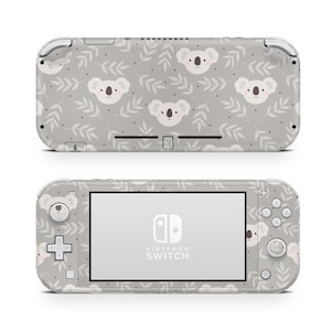 Pode incluir: Um console Nintendo Switch Lite cinza com um padrão de coala e folhas. O console tem um logotipo branco do Nintendo Switch e o texto "NINTENDO SWITCH".