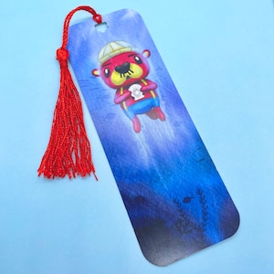 Peut inclure: Une loutre de dessin animé rouge et blanche portant une tenue de marin bleu et blanche et tenant une coquille Saint-Jacques. La loutre nage dans un décor sous-marin bleu et violet avec un marque-page à glands rouge attaché.