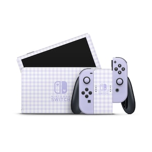 Może przedstawiać: Konsola Nintendo Switch i kontroler w fioletowo-białe kraty w kratkę z logo w kształcie serca. Konsola ma nadrukowany napis "Nintendo Switch".
