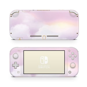 Puede incluir: Una consola Nintendo Switch Lite rosa y blanca con un diseño de nubes y puesta de sol. La consola tiene detalles dorados y el logotipo de Nintendo Switch es visible en la pantalla.