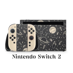 May include: A Nintendo Switch 2 console and controllers with a black and cream celestial design. The controllers are cream-colored with black buttons and a black grip. The console and controllers feature a pattern of planets, stars, and hand illustrations.