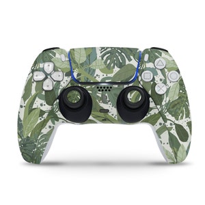 Puede incluir: Un mando de PlayStation 5 DualSense blanco con un patrón de hojas tropicales verdes y blancas.
