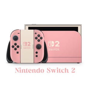 Puede incluir: Una consola Nintendo Switch 2 rosa con mandos a juego. Los mandos son rosas y crema con detalles en negro. La consola y los mandos tienen el logotipo de Nintendo Switch. El texto "Nintendo Switch 2" se muestra debajo.