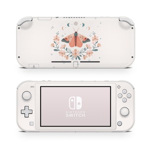 Puede incluir: Consola Nintendo Switch Lite blanca con un diseño floral y de mariposa en la parte posterior. El diseño presenta una polilla con alas rosadas y naranjas, rodeada de una corona de flores en tonos rosa, verde y azul. La parte frontal de la consola muestra el logotipo de Nintendo Switch y el texto.