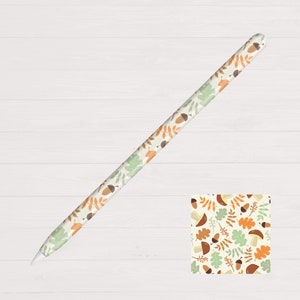 May include: A white Apple Pencil with a brown, green and beige pattern of leaves and acorns. The pattern is repeated on the pencil.