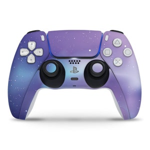 Può includere: Un controller PlayStation 5 viola e blu con una stampa a galassia. Il controller ha una piastra frontale bianca con il logo PlayStation e un touchpad bianco.