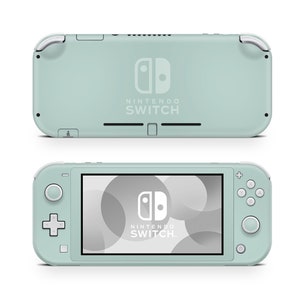 Może przedstawiać: Konsola do gier przenośna Nintendo Switch Lite w jasnozielonym kolorze. Konsola ma białe logo Nintendo i napis "Nintendo Switch" nadrukowany na tylnej części. Przednia część konsoli pokazuje zbliżenie ekranu z szarym i białym tłem.