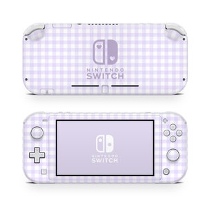 Puede incluir: Una consola Nintendo Switch Lite blanca con un patrón de cuadros vichy morado y blanco. El logotipo de Nintendo Switch está en la parte frontal de la consola.