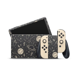 Puede incluir: Una consola Nintendo Switch negra y crema y dos mandos con un patrón celestial. El patrón presenta estrellas, lunas, planetas y manos.