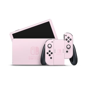 May include: A pink Nintendo Switch console with matching Joy-Con controllers. The console has the Nintendo Switch logo and the words "Nintendo Switch" printed on it. The Joy-Con controllers have black buttons and a pink exterior.