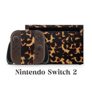 Puede incluir: Una consola Nintendo Switch 2 y sus mandos con un patrón de carey marrón y amarillo. El texto "Nintendo Switch 2" se muestra en la parte inferior de la imagen.