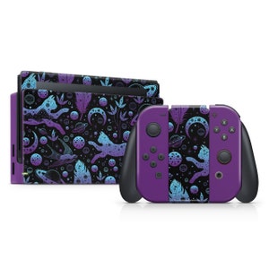Puede incluir: Skins para consola y mando de Nintendo Switch de color morado y azul con un patrón de temática espacial con gatos, lunas, planetas y plumas.