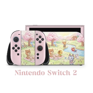 Puede incluir: Una consola Nintendo Switch 2 rosa con un diseño personalizado que presenta animales de dibujos animados en una escena de picnic. Los mandos Joy-Con son rosas con detalles y botones negros. La pantalla muestra un paisaje a juego.