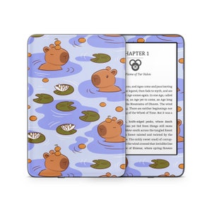 May include: A Kindle Paperwhite e-reader with a blue and brown patterned case featuring cartoon capybaras and lily pads. The screen displays the text "CHAPTER 1 Flame of Tar Valon" from a fantasy novel.