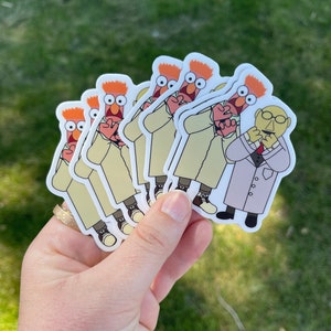 May include: A set of six stickers featuring a red-haired character in a white lab coat with a surprised expression. The character is holding a smaller character with a mustache and glasses in a lab coat. The stickers are printed on white paper.