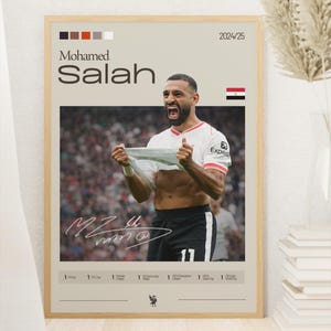 Op de afbeelding: Een poster met een foto van Mohamed Salah, een professionele voetballer, die een doelpunt viert. De poster is beige met zwarte tekst en een rode en witte voetbalafbeelding. De tekst op de poster luidt "Mohamed Salah" en "2024/25".
