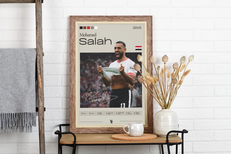 Op de afbeelding: Een ingelijste poster met een foto van Mohamed Salah, een voetballer, die een doelpunt viert. De poster heeft een bruine houten lijst en een witte achtergrond met de tekst "Mohamed Salah" en "2024/25" in zwart. De poster bevat ook een kleine Egyptische vlag.