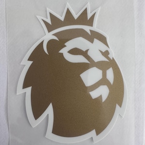 Könnte beinhalten: Ein gold-weißes Abziehbild mit dem Logo der Premier League. Das Logo zeigt einen Löwen mit Krone und weißer Umrandung. Der Aufkleber befindet sich auf einer transparenten Folie.
