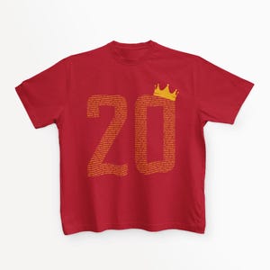 May include: Red t-shirt with a gold crown and the number 20 printed on the front. The number 20 is made up of small words.