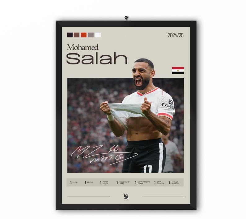 Op de afbeelding: Een ingelijste poster van Mohamed Salah, een professionele voetballer, die een doelpunt viert. De poster toont een foto van Salah in een wit en rood shirt, met de tekst "Mohamed Salah" en "2024/25" gedrukt op de poster. De poster bevat ook een handtekening en een kleine Egyptische vlag.