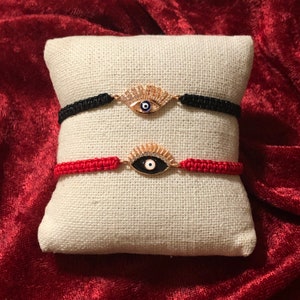 May include: Two evil eye bracelets with black and red string. The evil eye charms are gold with white and blue accents.