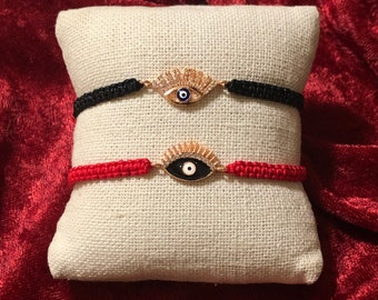 May include: Two evil eye bracelets with black and red string. The evil eye charms are gold with white and blue accents.
