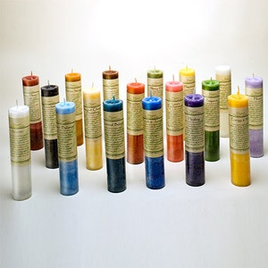 May include: A collection of cylindrical candles in various colors, including white, blue, green, and yellow. Each candle has a label wrapped around it. The candles are arranged on a white surface.