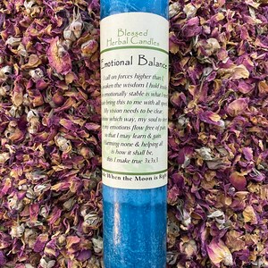May include: A blue pillar candle with the text "Emotional Balance" and "Blessed Herbal Candles". The candle is surrounded by dried rose petals. The candle has a label with a poem.