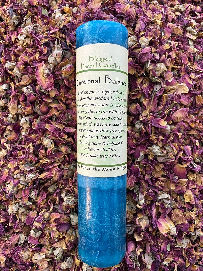 May include: A blue pillar candle with the text "Emotional Balance" and "Blessed Herbal Candles". The candle is surrounded by dried rose petals. The candle has a label with a poem.