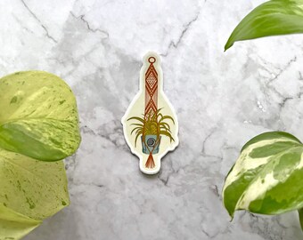 May include: A sticker of a macrame plant hanger with a potted plant. The hanger is made of brown and red string and the plant is green with a light blue pot.