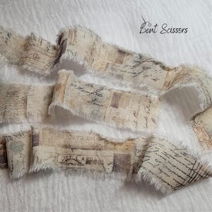 May include: Cream-colored fabric ribbon with a vintage postcard print. The ribbon has frayed edges and is printed with faded text and postage stamp designs. The words "Bent Scissors" are written in cursive on the top right.