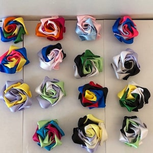 May include: Assortment of 16 handmade fabric roses in various colour combinations. Each rose is made from multiple layers of satin ribbon, creating a layered and dimensional effect.