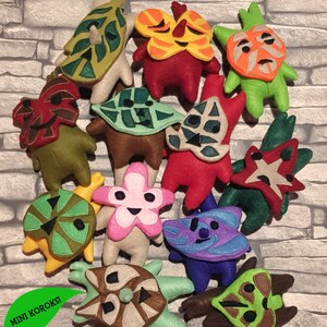 May include: A collection of 12 handmade felt plushies, each depicting a different character from the video game "The Legend of Zelda: Breath of the Wild". The plushies are all different colors and have unique designs, including a flower, a leaf, and a star.