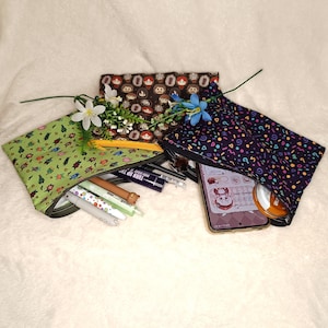May include: Three fabric zipper pouches with various patterns. One is green with a repeating pattern of blue and yellow figures, another is brown with cartoon faces, and the third is dark blue with colourful confetti shapes.
