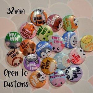 May include: A collection of 32 mm button badges featuring various animal illustrations and pronoun phrases, including "She/Her", "He/Him", "They/Them", "All Pronouns", and "Any Pronouns".