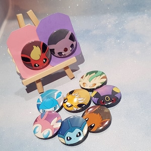 May include: Eight colourful round buttons featuring different Pokemon characters. The buttons are arranged in a circle on a light blue sparkly surface.