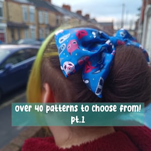 May include: A person with yellow and brown hair wearing a blue and red patterned hair bow. The bow has a variety of designs, including masks, stars, and other geometric shapes. The text "over 40 patterns to choose from! pt.1" is visible in the image.