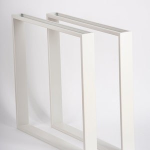 May include: Two white metal table legs, each with a square frame. The legs are positioned side by side, with one slightly in front of the other.