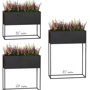 May include: Three black metal planter boxes with stands. The planter boxes are 35 cm wide, 60 cm wide, and 85 cm wide. Each planter box is filled with pink flowers.