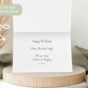 May include: A white greeting card with the message "Happy Birthday!" and a personal note. The card is open, revealing the message inside. The card is on a wooden stand with decorative elements.