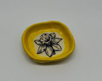 Plato artesanal de cerámica amarilla esmaltada con diseño de narcisos negros: una pieza decorativa original.