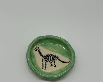 Plato artesanal con forma de esqueleto de dinosaurio y borde esmaltado en verde.