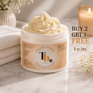 May include: A white plastic jar filled with off-white organic whipped shea butter. The label features the text "Organic Whipped Shea Butter" and "Tee's Better Butters". The text "BUY 2 GET 1 FREE 8 oz Jars" is printed to the right of the jar.