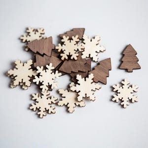 May include: A collection of wooden Christmas ornaments, including snowflakes and Christmas trees. The snowflakes are light-colored, while the trees are a darker brown. These ornaments are ideal for holiday crafts and decorations.