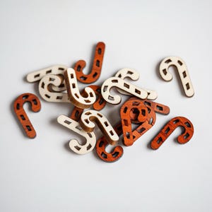 May include: A pile of wooden candy cane shapes in brown and white. The candy canes are scattered on a white surface.