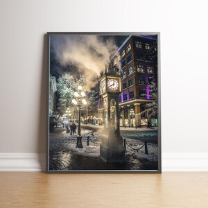 May include: A vintage clock tower with a clock face and a steam plume rising from the top, located on a snowy street in a city at night. The street is lined with streetlights and buildings.