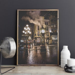 May include: A framed wall art print depicting the Gastown Steam Clock in Vancouver at night. The scene features the iconic clock emitting steam, illuminated street lamps, and wet cobblestone streets in a dark, atmospheric urban setting.